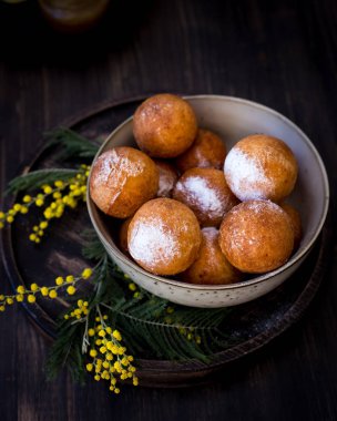Pudra şekeri ile bir tabak çörek üzerinde Mimoza çiçeklerle süslenmiş. Ahşap arka plan