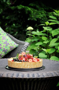 Doğa meyve pasta çilek ve diğer meyveler ile yeşil bir bahçe içinde. Dokuma masaya