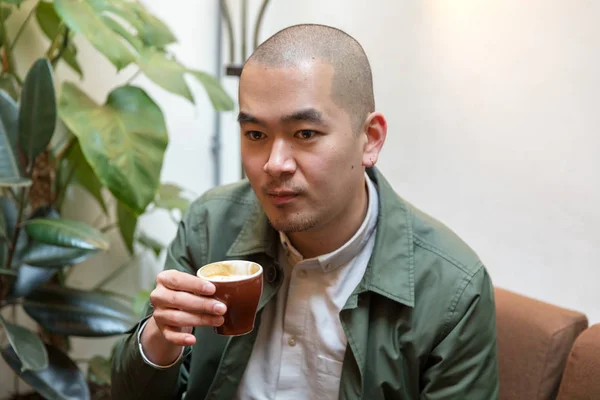 Chinesischer junger Mann mit Ohrring im Café mit Mütze — Stockfoto