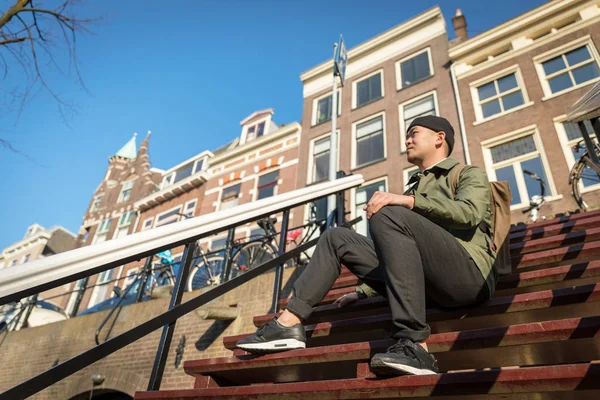 Urban asiatisk man med ryggsäck sitter på trappan. Snygg. C — Stockfoto