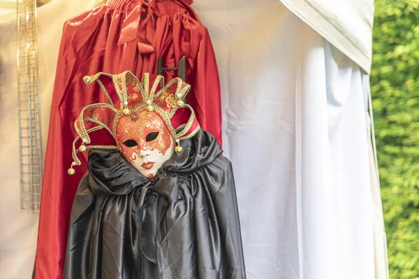 Máscara de traje veneciano y capas rojas y negras contra la espalda blanca —  Fotos de Stock