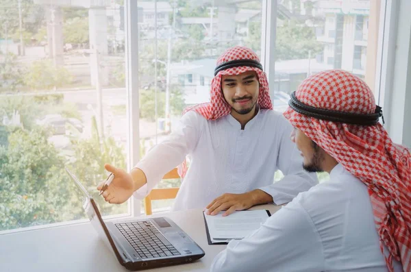 two young Arabian business man showing presentation and share idea of new project with laptop computer and clipboard on desk in office, coworker, successful, partnership, teamwork, positive, concept