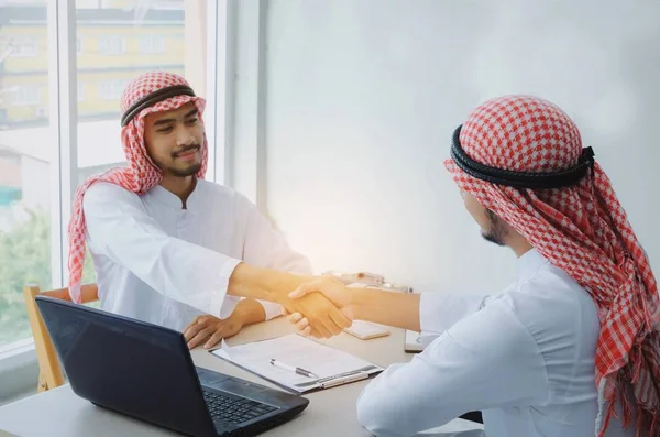 two young Arabian business man handshake with laptop computer and clipboard on desk after finishing up a business deal meeting contract in office, coworker, successful, partnership, teamwork concept