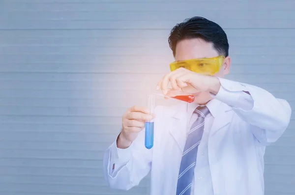 asian man scientist in protective glasses working and dropping red liquid substance into blue liquid in chemical laboratory lab, science, chemistry, biology, pharmacy, medical research concept