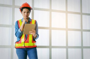 düşünme teknisyen veya mühendis Asyalı kadın kask ile yansıtıcı kılığına girmiş ve inşaat alanında, mimar, mühendis, güvenlik, sanayi ve inşaat kavramı binada tablet