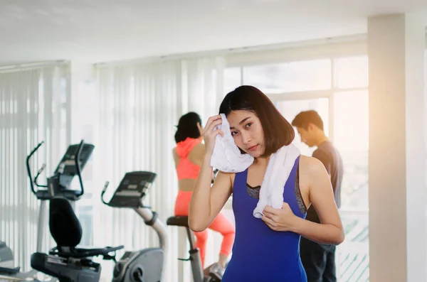 young asian pretty woman wipes sweat with towel while resting after workout for good healthy with people in fitness gym, bodybuilder, healthy lifestyle, exercise fitness and sport training concept