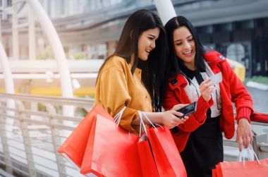 iki güzel neşeli Asya ve beyaz genç kadın ile mobil akıllı telefon, kredi kartı ve holding alışveriş birlikte modern şehir, satış, insanlar, ödeme ve online kavramı alışveriş torbaları