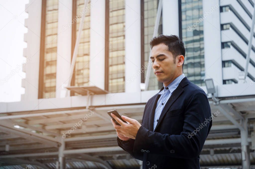 young smart asian business man wearing modern black suit with mobile smart phone in building city background, successful, internet network connection, technology communication, financial concept