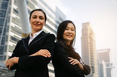 iki gülümseyen iş Asya ve beyaz kadın resmen modern şehir, kendine güvenen, ayakta geçti kollarını ile kameraya bakarak giyinmiş takım lideri, başarılı ve Girişimcilik kavramı