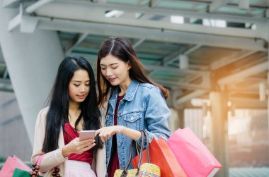 iki güzel neşeli Asya genç kadınla birlikte modern şehir, kış indirimi, siyah Cuma, promosyon, Özel Fırsat Satış, ödeme online kavram yürümeye poşetler tutarak mobil akıllı telefon
