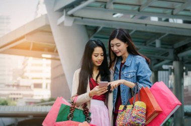 iki güzel neşeli Asya genç kadınla birlikte modern şehir, kış indirimi, siyah Cuma, promosyon, Özel Fırsat Satış, ödeme online kavram yürümeye poşetler tutarak mobil akıllı telefon