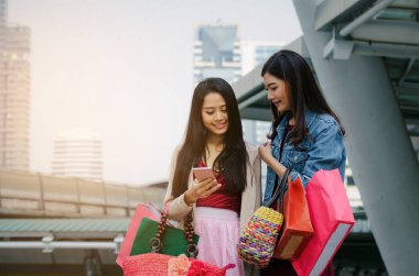 iki güzel neşeli Asya genç kadınla birlikte modern şehir, kış indirimi, siyah Cuma, promosyon, Özel Fırsat Satış, ödeme online kavram yürümeye poşetler tutarak mobil akıllı telefon