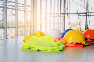 Masa başında, sanayi ve inşaat yapı kavramı Emanet mühendis inşaat mevcuttur ve İskele arka plan üzerinde yansıtıcı giysi ile beyaz, turuncu, sarı ve mavi güvenlik kask