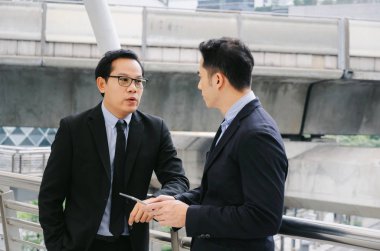 iki iş Asya akıllı adam konuşuyor ve finans haberleri içinde hareket eden hakkında bilgi okuma elbiseli tablet birlikte ayakta modern şehir, ağ teknolojisi, Internet, başarılı, ekip çalışması kavramı