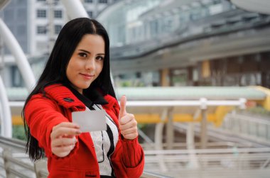 kredi kartı tutan ve başparmak gösterilmesini modern büyük şehir, moda, promosyon, kampanya, kış indirimi, insanlar, ödeme, alışveriş online kavramı kırmızı ceketli güzel neşeli bir genç kadın