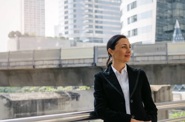 portrait of medium aged smart caucasian business woman wearing modern black suit standing in building city background, confident, team leader, successful, manager and entrepreneurship concept