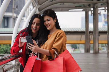 iki güzel neşeli Asya ve beyaz genç kadın ile mobil akıllı telefon, kredi kartı ve holding alışveriş birlikte modern şehir, satış, insanlar, ödeme ve online kavramı alışveriş torbaları