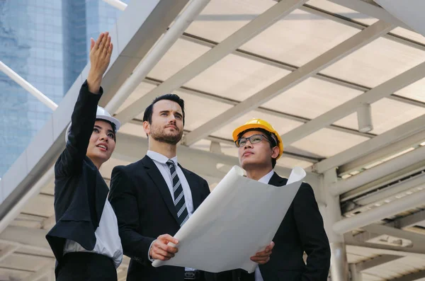 Grup iş ya da mühendis kadın ve yeni proje, başarılı konsepti başlangıç planlama adam kask ve binaya yukarıya bakıp modern şehir, çalışmalarını kontrol planı
