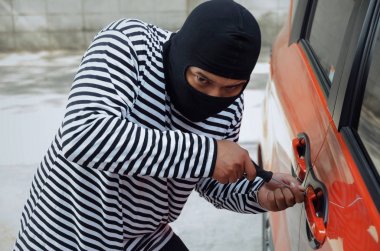 büyük şehirde sokakta araba çalmak için arabanın kapısını açmak için tornavida kullanarak siyah ve beyaz ceketli hırsız araba suç soyguncu break ve kavram çalmak