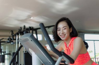 Asya genç güzel kadın ince vücut için iyi sabah, vücut geliştirme uzmanı, yaşam tarzı, egzersiz fitness, egzersiz ve spor kavramı sağlıklı fitness salonunda bisikletle eğitim kardiyo egzersiz gülümsemek