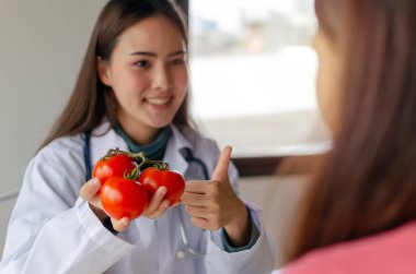 Besleyici bir şey. Dost canlısı diyetisyen kadın doktor hastanedeki genç hastaya taze kırmızı domates ve sebzeyle onay veriyor. Beslenme, diyet, gıda bilimi, sağlıklı gıda kavramı.