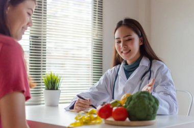 Besleyici bir şey. Dost canlısı diyetisyen kadın doktor gülümseyen ve diyet planı hakkında tartışan ofis hastanesindeki genç hastaya, beslenme, gıda bilimi, sağlıklı gıda konsepti