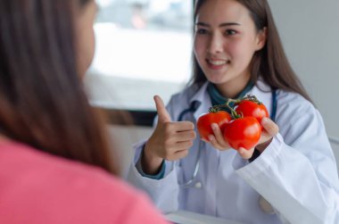 Besleyici bir şey. Dost canlısı diyetisyen kadın doktor hastanedeki genç hastaya taze kırmızı domates ve sebzeyle onay veriyor. Beslenme, diyet, gıda bilimi, sağlıklı gıda kavramı.