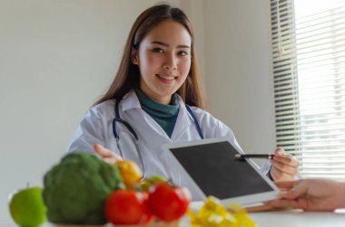 Besleyici bir şey. Güzel, dost canlısı, doktor, tabletli, diyet planından bahseden bir doktor. Ofisteki genç hastaya sebze, beslenme, gıda bilimi, sağlıklı gıda konsepti.