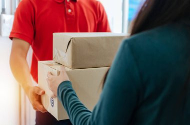 Genç bayan müşteri evden paket posta kutusu alıyor, kırmızı üniformalı ev teslimatçısı, ekspres teslimat servisi, kargo taşımacılığı, ulaşım lojistiği ve online alışveriş konsepti.