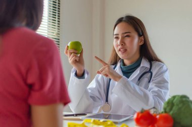 Dost canlısı diyetisyen kadın doktor, yeşil elma ve sebzeli diyet planından ofis hastanesindeki genç hasta kadına, beslenme, gıda bilimi, beslenme, sağlıklı gıda konseptine bahsediyor.