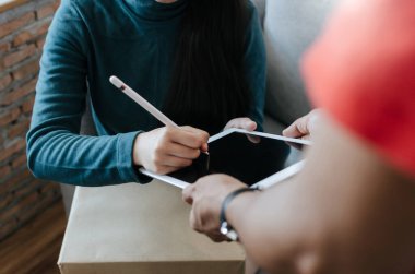 Kadın müşteri, dijital tabletle imzalaması için kırmızı üniformalı kalem teslimatçısı alır. Evdeki kuryeden paket posta kutusu, ekspres teslimat ve online alışveriş kavramı alır.