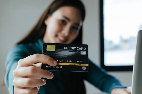 asian young pretty woman showing and paying with credit card and laptop computer on desk at home office, internet technology, electronic online booking, digital payment and shopping online concept