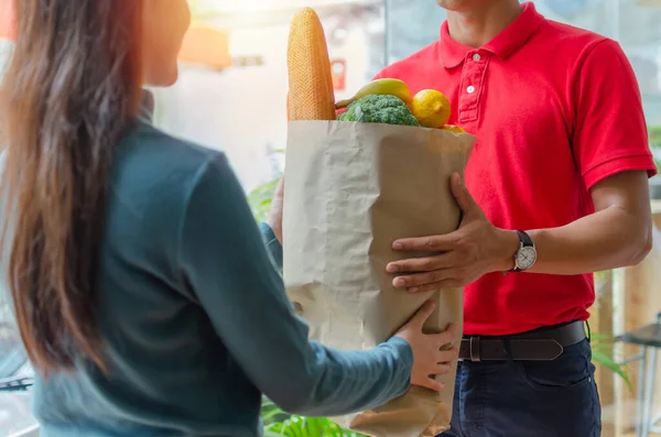 kırmızı üniformalı akıllı gıda dağıtım servisi adam alıcı ve genç kadın müşteri evde kurye sipariş alma taze gıda teslim, ekspres teslimat, gıda teslimat, online alışveriş konsepti