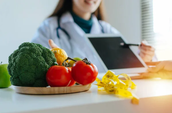 focus fresh vegetables and fruits with nutritionist female doctor using tablet and talking about diet plan with patient on desk at office hospital, food science, healthy food and dieting concept