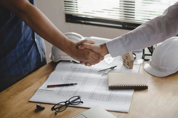 engineer, interior designer and architect hands shaking greeting start up plan new project contract with blueprint on desk in meeting room office at construction site, partnership, contractor concept