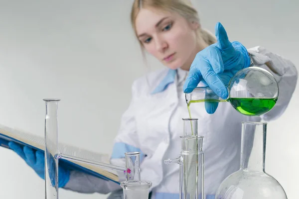 chemist girl in a white coat on a light background, pours something from a test tube