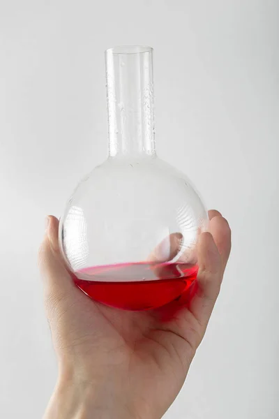 Hand holds flask with red liquid on a white background