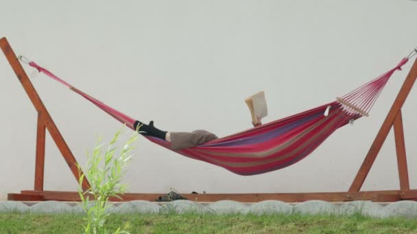 Relajado hombre leyendo libro en una hamaca — Vídeo de stock