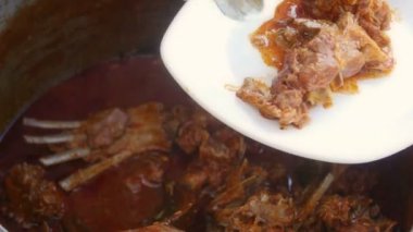 Kuzu güveç büyük bir metal tencerede pişirilir ve polenta ile servis edilir