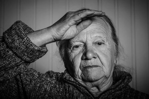 Portrait of an elderly woman with hand near face on a light back — Stock Photo, Image