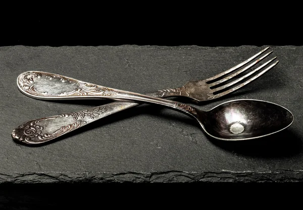 Vidlička a lžíce na talíři břidlice na černém pozadí. Tónovaný — Stock fotografie