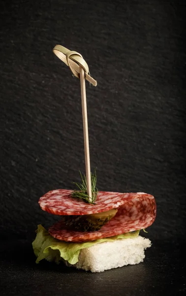 Pequeños bocadillos canapé con salami, pan y lechuga en pincho en —  Fotos de Stock