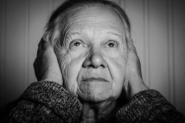 Portrait of an elderly woman with hands near face on a light bac — Stock Photo, Image