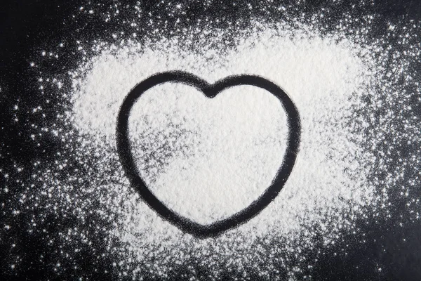 Forma de coração desenhado sobre a farinha em um fundo preto — Fotografia de Stock