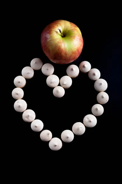 Pequeñas galletas colocadas en forma de corazón y manzana madura en negro — Foto de Stock