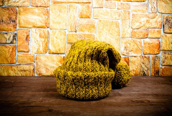 Sombrero de punto hecho a mano en una mesa de madera oscura frente a la pared de piedra . —  Fotos de Stock