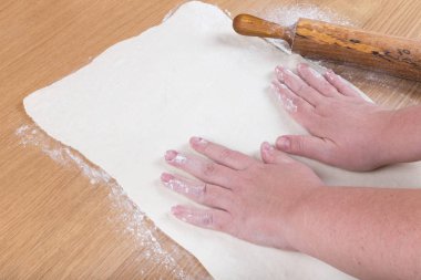 Dolgun kadınların elleri ile hamur hafif ahşap bir masa üzerinde çalışmak.