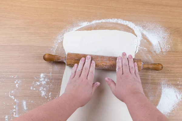 Dolgun kadınların elleri ile hamur hafif ahşap bir masa üzerinde çalışmak.
