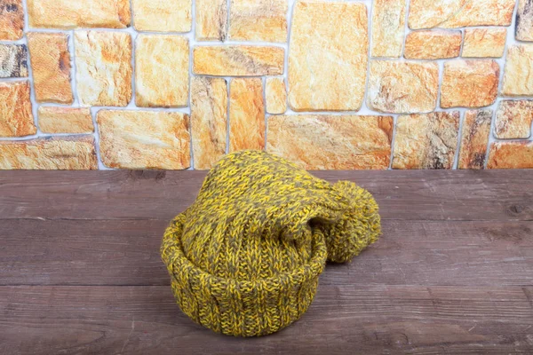 Handmade knitted hat on a dark wooden table opposite stone wall — Stock Photo, Image