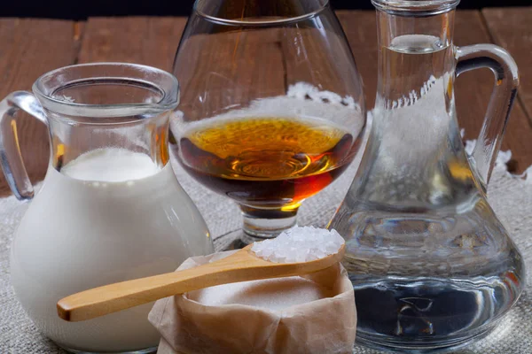 Cognac in a glass goblet, milk, water, sugar and salt in wooden — Stock Photo, Image